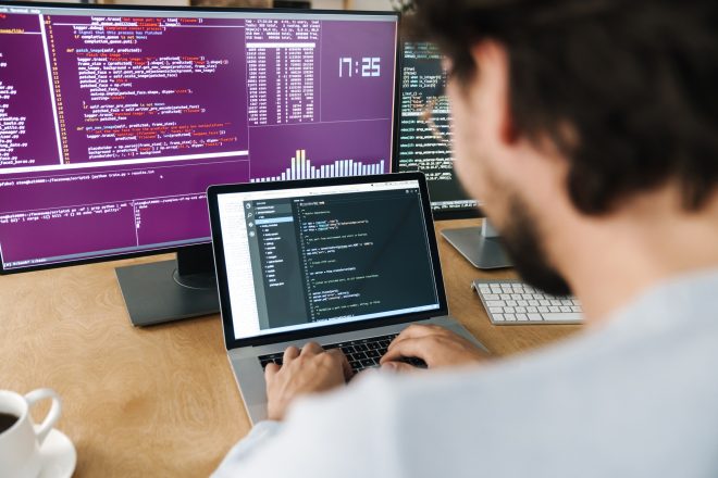 Image of focused caucasian programmer man working with computers