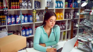 Saleswoman working on laptop in auto parts store managing inventory